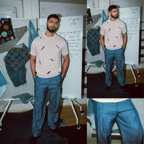 Man wearing a beige t-shirt with black patterns and blue pants in a room with fabric samples.