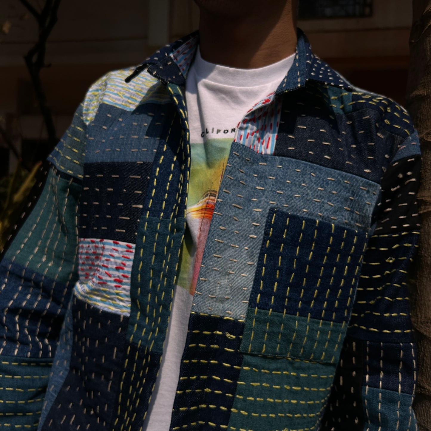 A person wearing an Indigo Weave Jacket with Kantha embroidery patches in various shades of blue and colors.