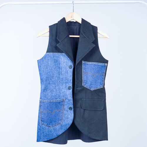 A denim sleeveless jacket hanging on a hanger, with a mix of solid navy blue and blue denim fabric.