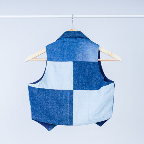 A denim vest with a structured, geometric design, displayed on a hanger against a white background.